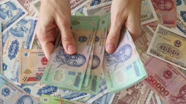 Close up view of hands counting stack of Vietnamese dong paper money bills in Vietnam. Concept of financial accounting, wealth, business budget calculation, domestic cash expenses and income tax.