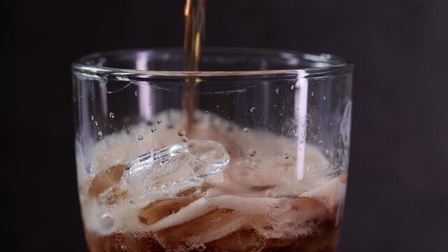 Close-Up Cola Pouring into Glass with Ice Cubes Creating Bubbles and Foam, Refreshing Cold Drink Concept