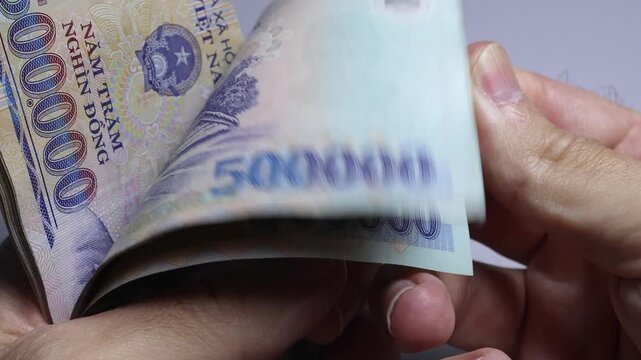 Close up view of hand flipping through stack of 500000 Vietnamese dong paper money bills in Vietnam. Concept of dynamic cash counting, business profit calculation, income and high wealth.