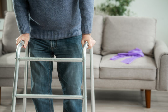 Senior man sitting on a sofa and using a walker at home, showing mobility support, recovery, aging, and daily care in a bright living room.