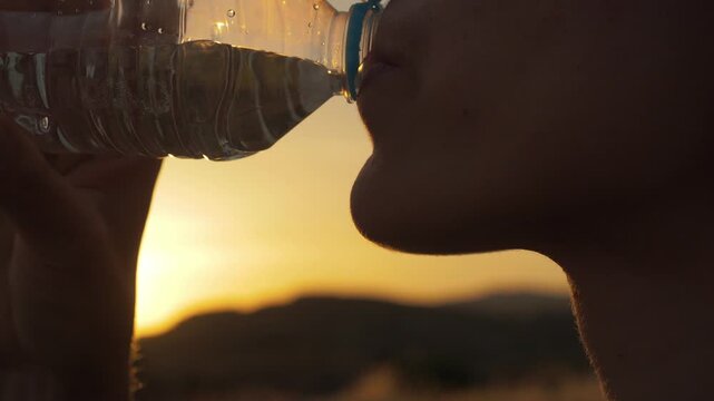 Person drinking from a bottle, savoring refreshment and rejuvenation during a serene outdoor sunset escape, perfect for wellness and outdoor campaigns.