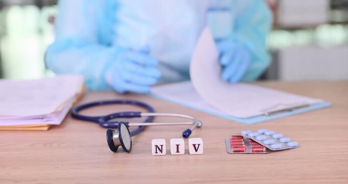 Lab specialist studies medical test results and prescribes treatment. Small cubes on table form abbreviation NIV near stethoscope and tablets