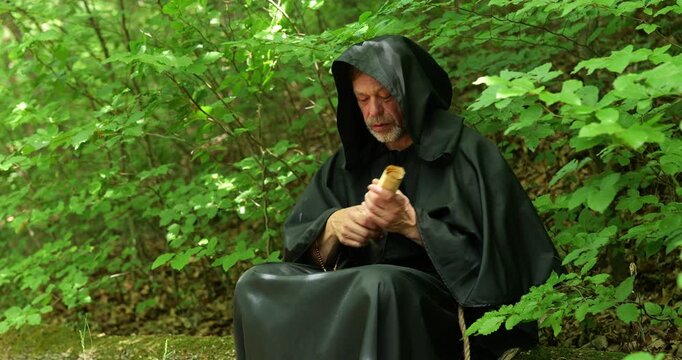 Monk sits in the forest and takes out a scroll for reading or study during a solitary religious journey