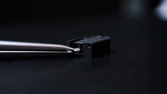 Metal tweezers inserting a white strip into a small black component