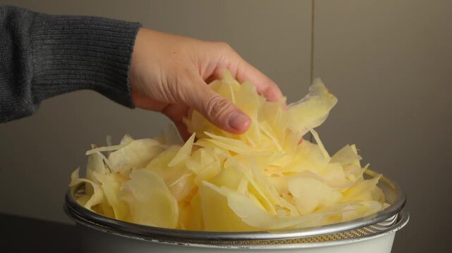 A person holding and draining thinly sliced raw potatoes before deep frying