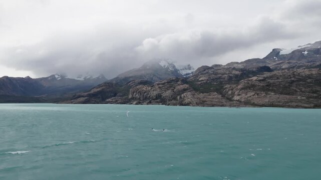 Lago Argentino, Santa Cruz, Argentina, featuring wind driven glacial waters, granite mountain ranges, snowfields and storm clouds within Los Glaciares National Park, onboard navigation shot.