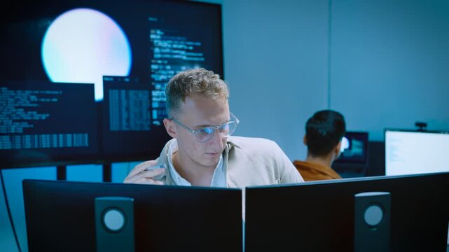 Focused young male programmer spinning pen while thinking of software coding and AI system development on computer in tech office