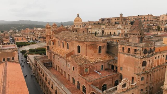 Drone panoramic shot over Noto, Italy. The aerial footage captures the historic baroque architecture, San Domenico church, and the iconic Cathedral under a cloudy sky, Sicily