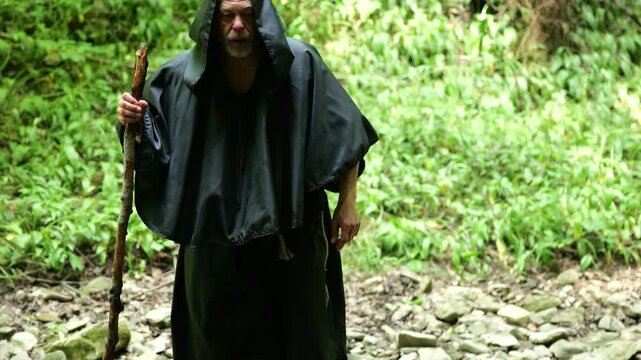 Monk finishes crossing a rocky stream and continues his journey through forest terrain.