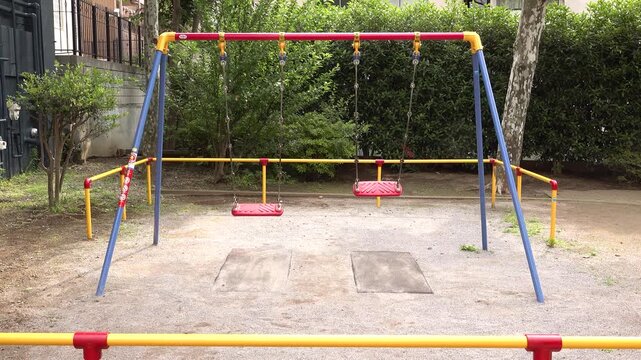 Empty red double swings in a small Japanese urban park