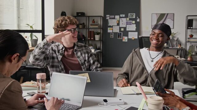 Caucasian and African American young programmers sitting at desk, discussing code on laptops and celebrating with fist bump. Video for IT startup marketing and tech teamwork ads