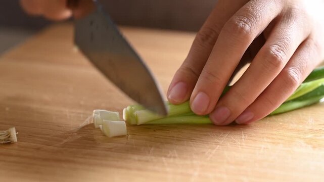 Close-up of woman hand holding kitchen knife and chopping fresh spring onion on wooden cutting board