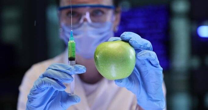 Woman scientist nutritionist holds green apple near syringe in lab. Gloved hand releases extra air preparing liquid dose for food testing work
