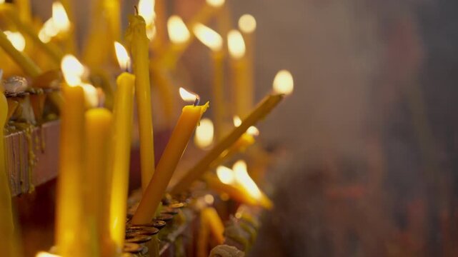 A close-up image of a cluster of candlelight illuminating a prayerful scene, set against a beautiful bokeh effect of candlelight flames and rising incense smoke during a candlelit procession.