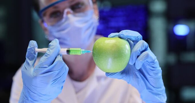 Woman scientist tests green apple with syringe in lab. Gloved hand guides needle toward fruit preparing food sample injection carefully slow motion