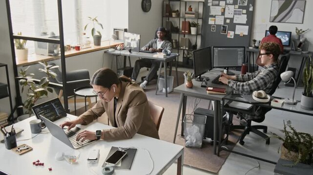 Multiethnic young programmers working on computers in modern open-plan office. Footage for software development company promos, IT recruitment, and tech startup advertisements
