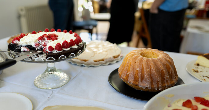 Authentic assortment of homemade cakes and berry desserts displayed on serving table during casual social event with warm lifestyle atmosphere
