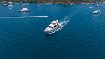 Naklejka premium Luxury Yacht Cruise: A sleek white yacht cuts through the deep blue ocean, leaving a wake of white foam as other boats dot the horizon under a clear sky.