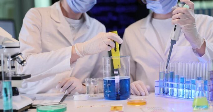 Women chemists wearing protective gear research blue liquid in lab. Scientists colleagues conduct tests of water with digital tools at workplace