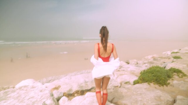 Contemplative woman in swimsuit and skirt on rocky coastline