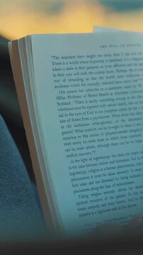 A person gently turns the pages of a philosophical book while reading in soft indoor lighting.