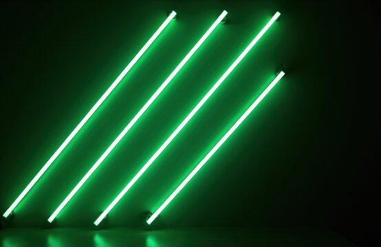 Diagonal bright green neon tube lights glow on dark wall. Modern abstract background with parallel lines of illumination. Simple geometric pattern creates futuristic atmosphere.