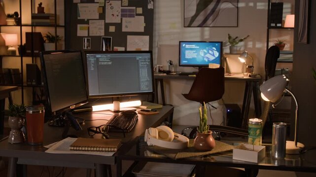 Empty workstations in IT office displaying software code on dual monitors at night. Video suits commercial projects about software development, cybersecurity, or overtime work