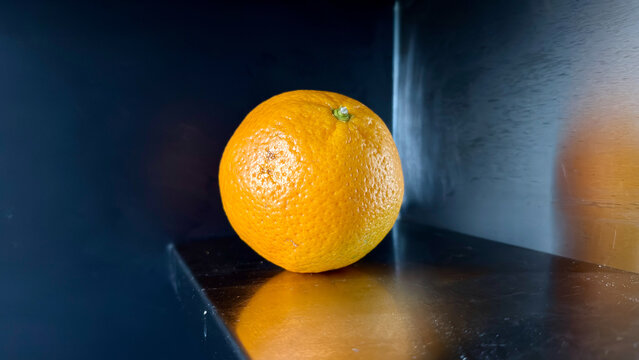 Single fresh orange fruit on dark kitchen counter close up
