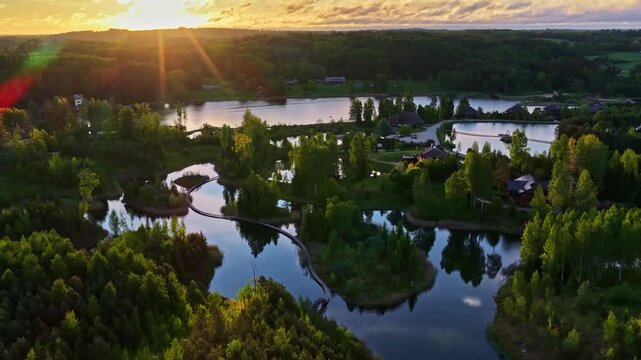 Scenic sunset above Latvian lakes, forest, homes, and winding pathways.