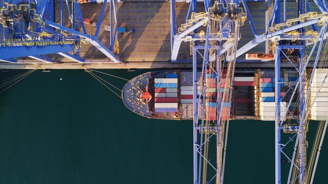 Stunning top-down aerial perspective showing a large cargo container ship maneuvering alongside the dock, with massive cranes ready for loading and unloading operations in a busy harbor