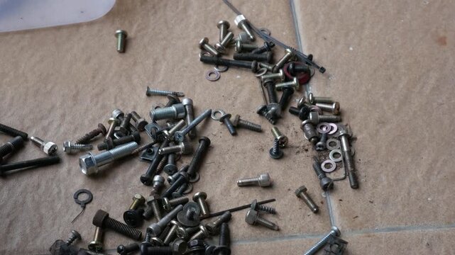 Hands Gathering Mixed Screws, Bolts and Nuts from Floor