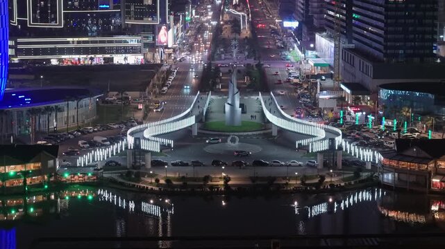 Capture of frozen Fountain Square in Batumi revealing illuminated modern buildings behind, showcasing a vibrant winter cityscape with glowing lights and urban atmosphere.