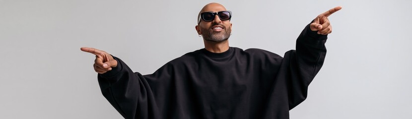 Obraz premium Confident man wearing sunglasses and black oversized sweatshirt pointing both directions for banner and social media background and promotional poster design