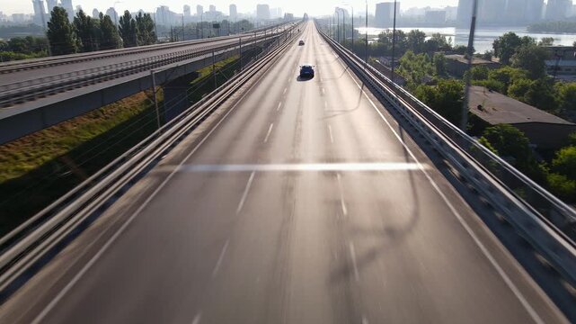 Morning traffic on a large multi lane highway bridge leading to the city under the rays of the rising sun
