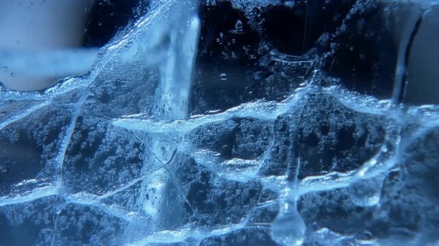 Slow motion close up of water droplets splashing and dripping on textured ice surface in studio cold indoor macro shot captured with controlled lighting