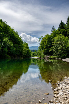 Vertical view of the emerald Kupa River with forest reflections and dramatic clouds creating a peaceful ecotourism scene along the Slovenia Croatia border