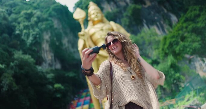 Woman takes selfies at Batu Caves in Malaysia with large statue in background during sunny day