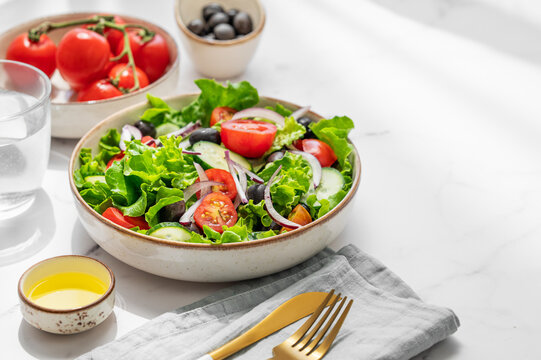 A fresh salad of tomatoes, cucumbers, lettuce, red onions, and olives on a plate