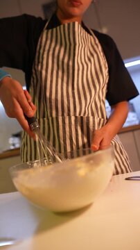 Focused woman stirring thick batter with big whisk in kitchen