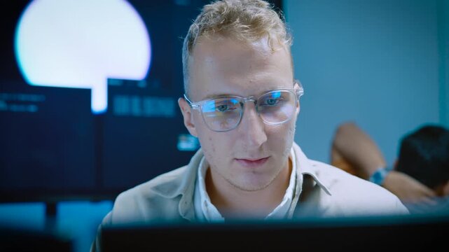 Close up of focused young male IT specialist typing and reviewing code on computer monitors while developing AI software system