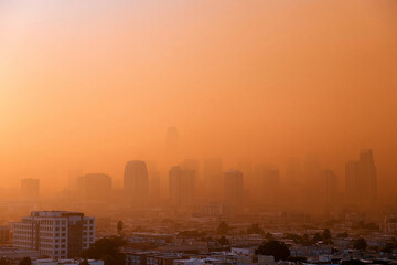 Obraz premium Orange haze blankets city skyline. Buildings fade into smoky glow. Urban sprawl shrouded in heat. Dusk or dawn, atmosphere heavy. Photograph captures environmental distress. Use for climate change