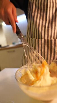 Closeup of whisk incorporating yolks into batter in warm lighting