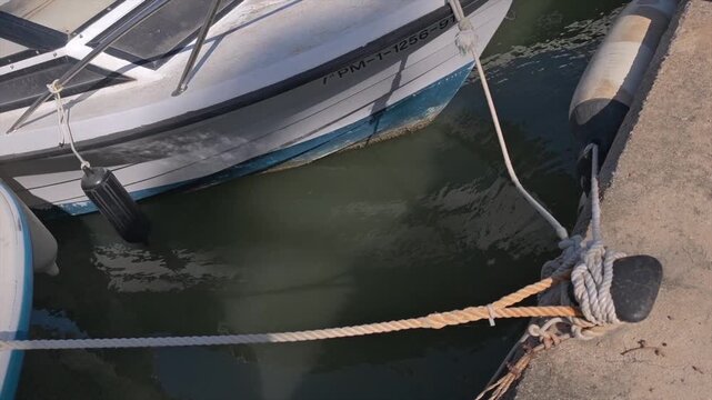 Horizontal shot of fishing boat moored to bollard with ropes and morning light reflections in harbor