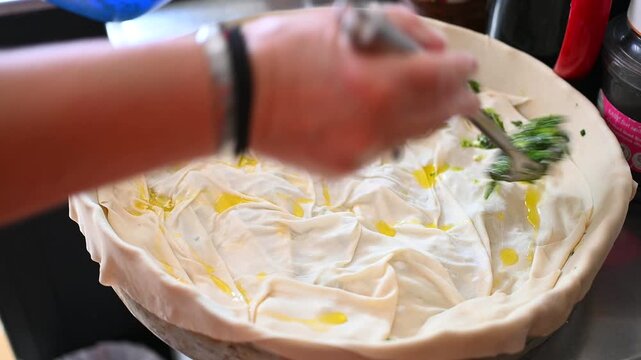 Spreading Fresh Herb and Feta Filling over Layered Phyllo Dough for Traditional Greek Spanakopita Preparation