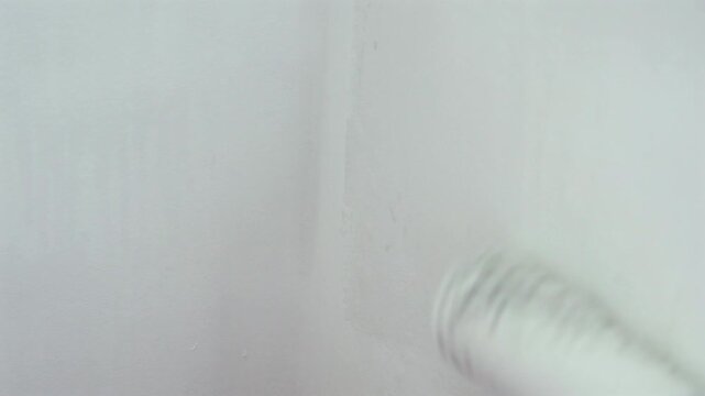 Blurred Paint Roller Applying White Paint to Wall. Out of focus close-up of a paint roller applying white paint to a wall. Abstract home renovation background with soft blur and copy space.