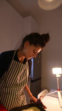 Concentrated woman uses oven mitts to place tray in oven for baking