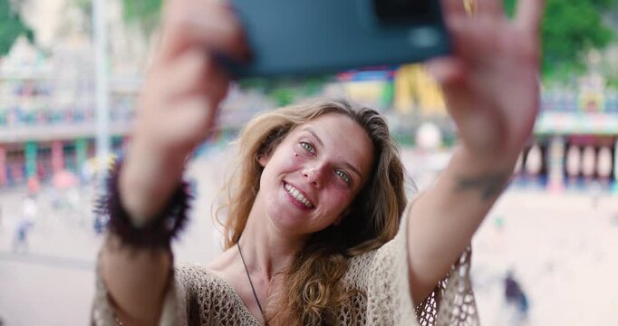 Girl takes selfies at Batu Caves in Malaysia during daytime bright colors and tourist crowd in the background capturing fun moments and enjoyable expressions