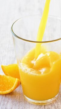 Pouring fresh orange juice into a glass with citrus slices on table, healthy breakfast beverage concept