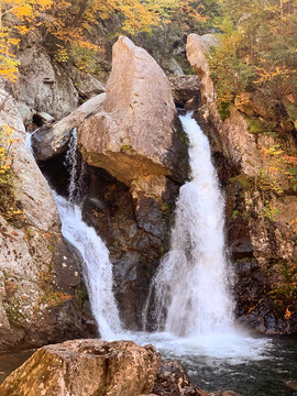 Bash Bish Falls plunges between massive granite boulders in the Berkshires of Massachusetts, surrounded by early autumn foliage and rugged mountain scenery.