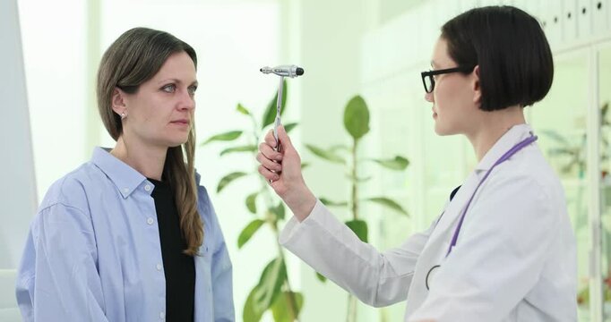 Doctor uses neurological hammer to check patient reactions in hospital. Female physician examines woman reflexes with tool in clinic slow motion